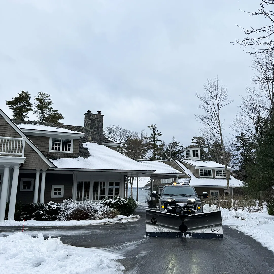 A truck plowing a driveway for snow removal service near me in Maine